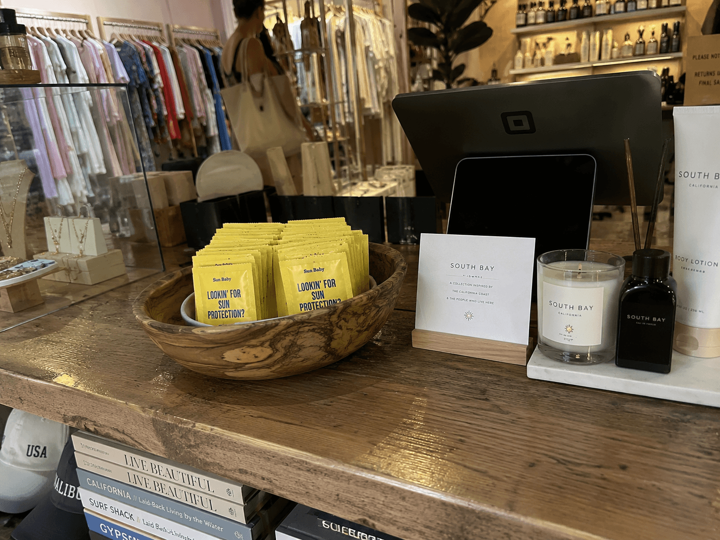 Boutique checkout counter with a wooden bowl of yellow Sun Baby packets beside the register
